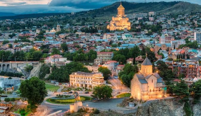 Vista panorâmica de Tbilisi 🇬🇪, capital da Geórgia, com suas ruas antigas, arquitetura moderna e o rio Kura ao fundo.